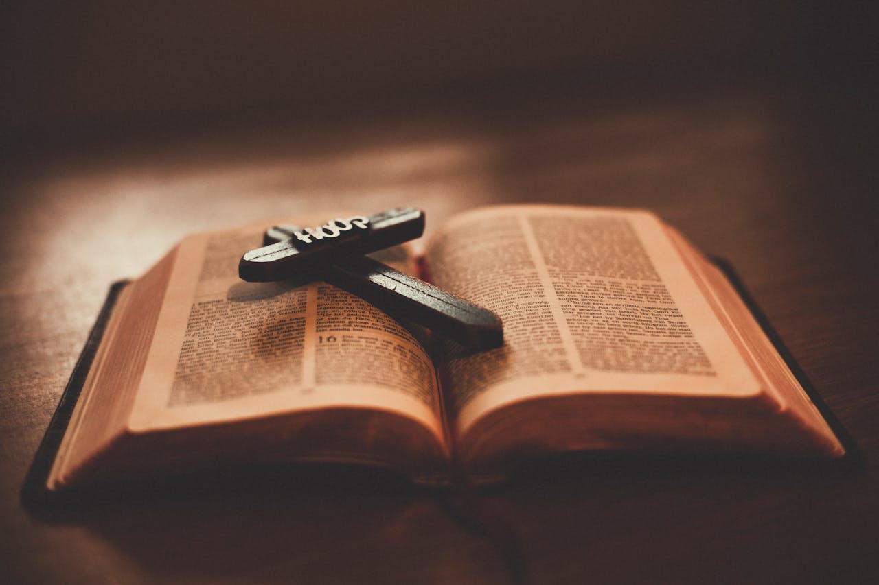 Home Close-up of an open Bible with a wooden cross inscribed with 'Hope' on a table.